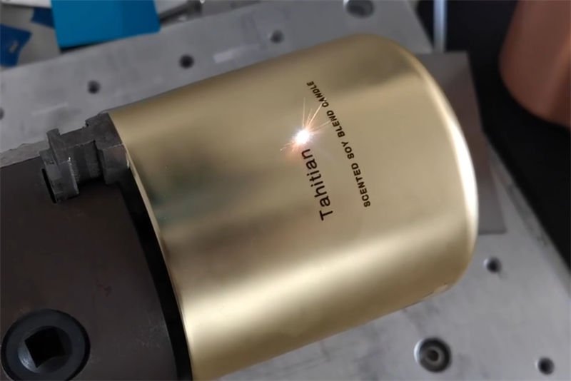 A fiber laser machine marking text on a gold-colored metal cylinder