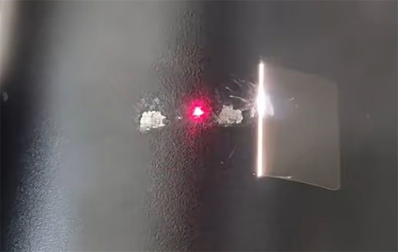 A laser beam cleaning paint off a metal surface, showcasing a red laser point and a reflective bright flash