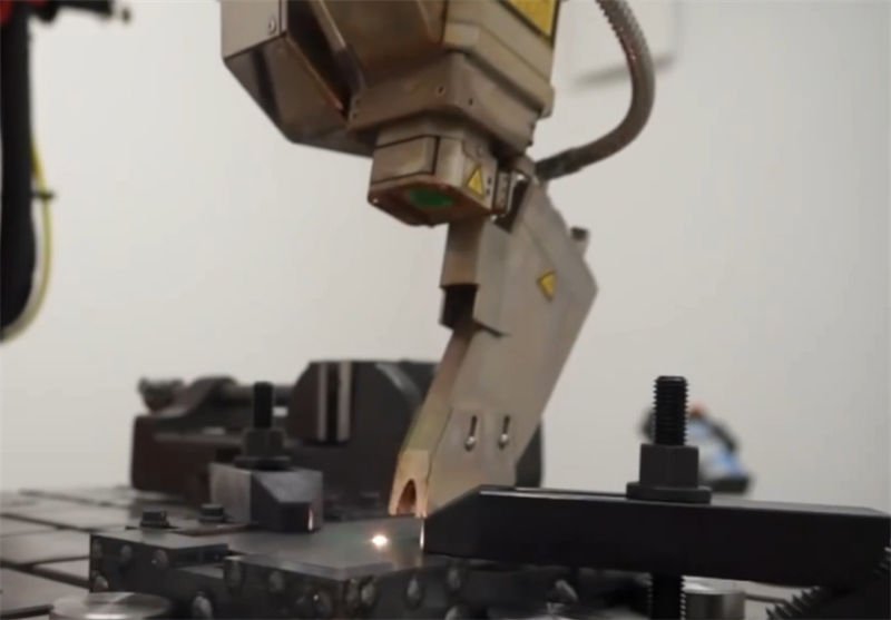 An industrial robot performing laser welding on a metal assembly in a manufacturing setting
