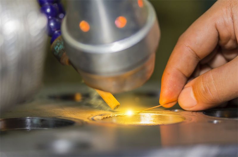 Close-up of a desktop laser welding setup, focusing on a precise weld being performed on a small metallic component