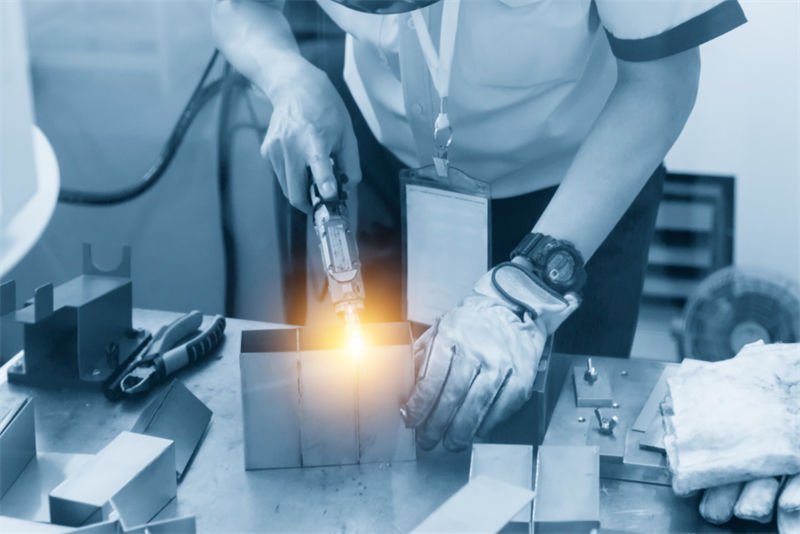 A worker using a handheld laser welding device on a desktop setup