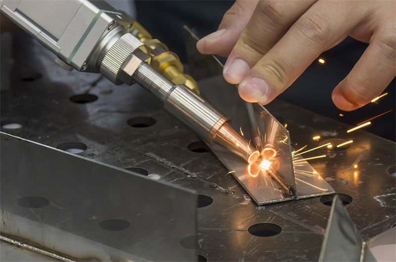 A close-up of a handheld laser welding gun in use, with sparks flying as it welds metal parts