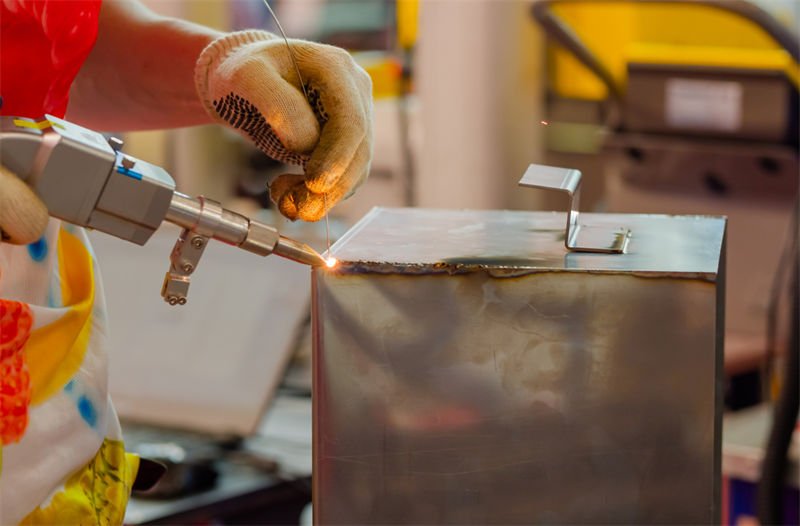 Precision Handheld Laser Welding in Industrial Application A worker using a handheld laser welding tool on a square metal container.