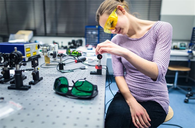 A woman wearing yellow laser safety glasses working on an optical testing bench with laser equipment