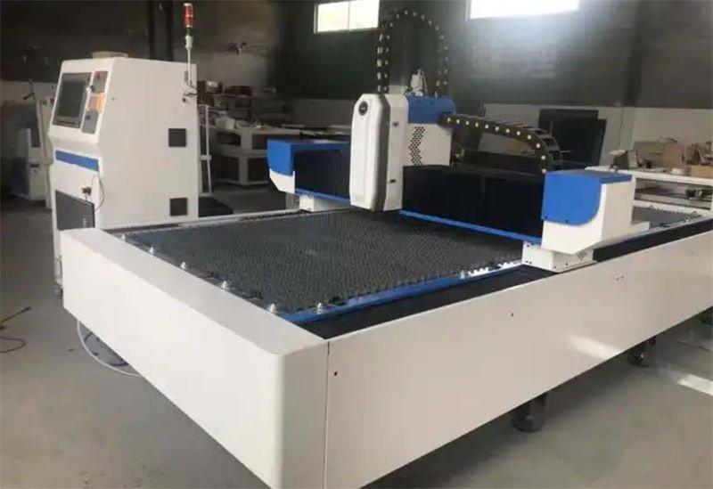 A laser cutting machine with a rectangular cutting bed and a computer control panel in an industrial setting