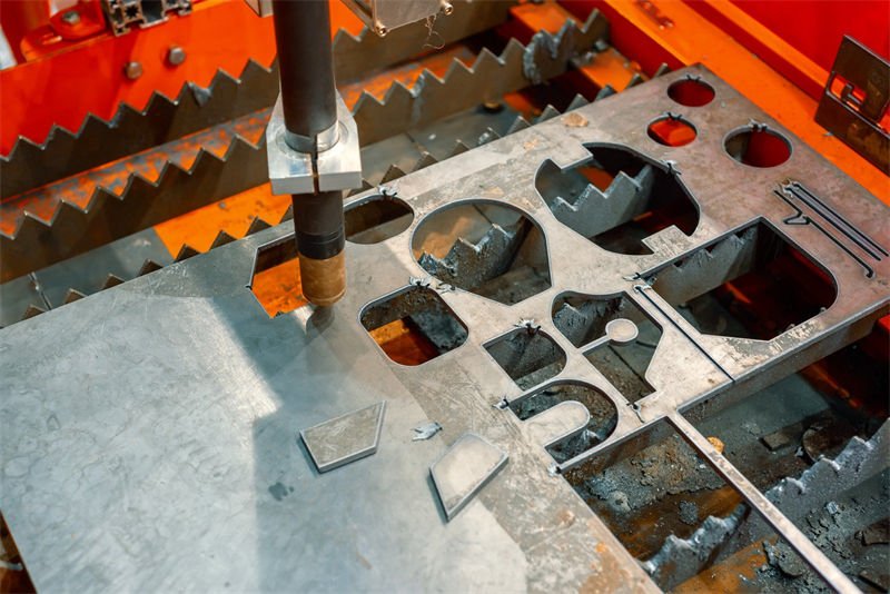 A plasma cutting machine creates intricate shapes in a stainless steel sheet, showcasing various cut-outs
