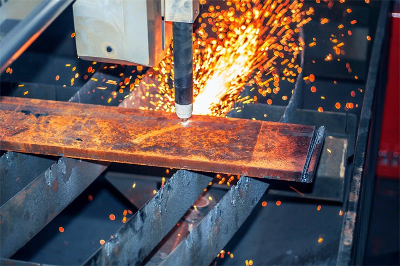 A plasma cutting torch showers sparks as it cuts through a heavily rusted steel beam.