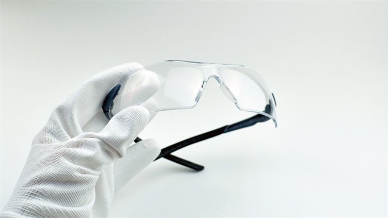 Laser Safety Glasses for Eye Protection A gloved hand holding a pair of transparent laser safety glasses with a white background