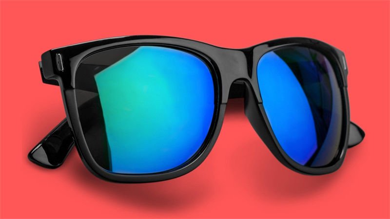 Stylish black-framed UV protection safety glasses with vibrant blue reflective lenses placed on a bright red background