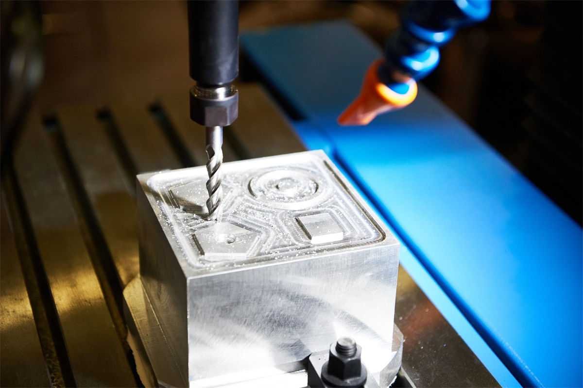 A CNC milling machine carving intricate designs on a metal block in a workshop setting