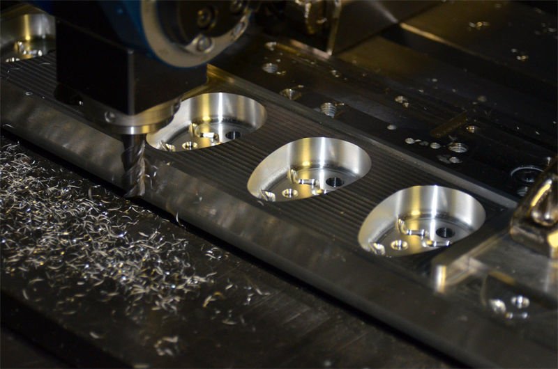 CNC machine in operation, milling circular depressions on a dark metal plate