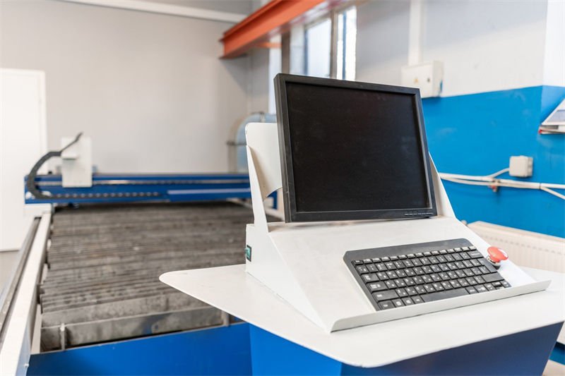 A control panel with a computer monitor and keyboard, part of a plasma CNC cutting machine in an industrial workshop.
