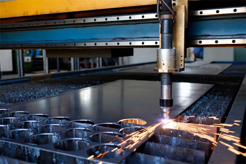 A plasma CNC cutting machine in action, cutting precise holes in a thin metal sheet with visible sparks