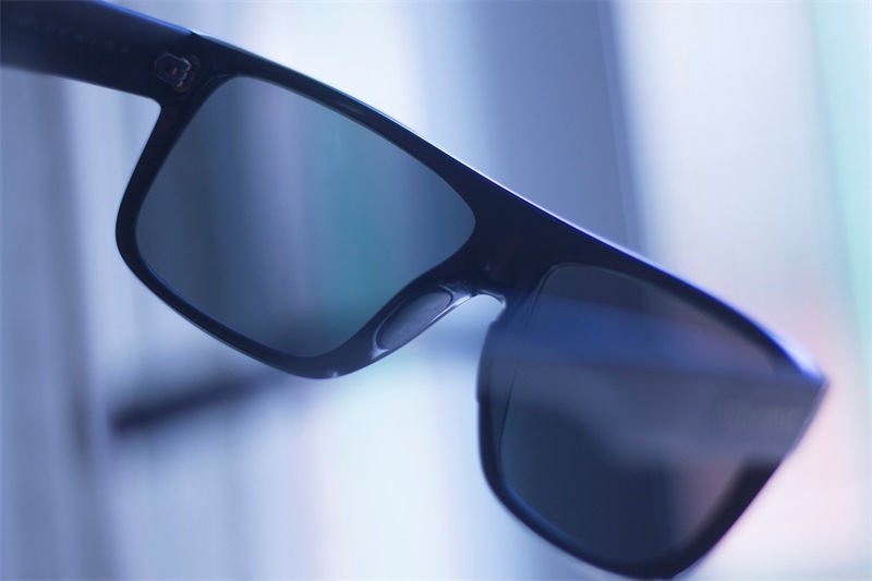 A pair of dark-tinted UV protection sunglasses held in front of a softly lit background, showcasing their light-blocking design
