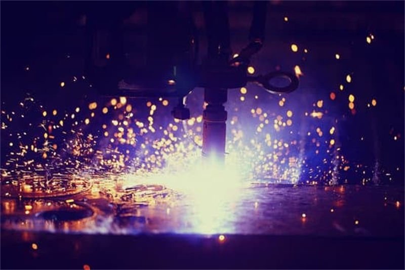 A plasma CNC cutting machine in a dark environment, emitting bright sparks and a glowing plasma arc while cutting metal.