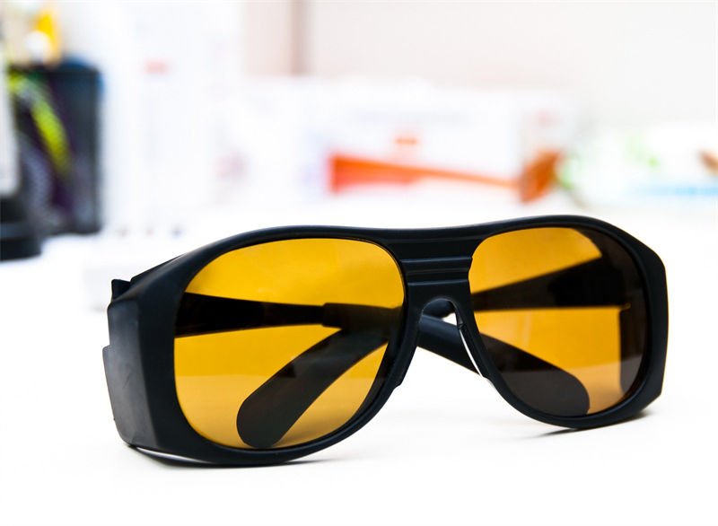 A pair of yellow-tinted protective glasses designed for 10600nm CO2 laser operations, placed on a white surface in a laboratory-like setting