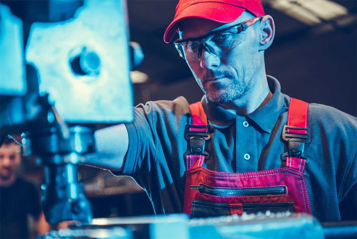 A technician wearing safety glasses and a red uniform performing maintenance on a CNC milling machine