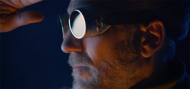 A man wearing reflective laser safety goggles in a dimly lit environment, looking focused