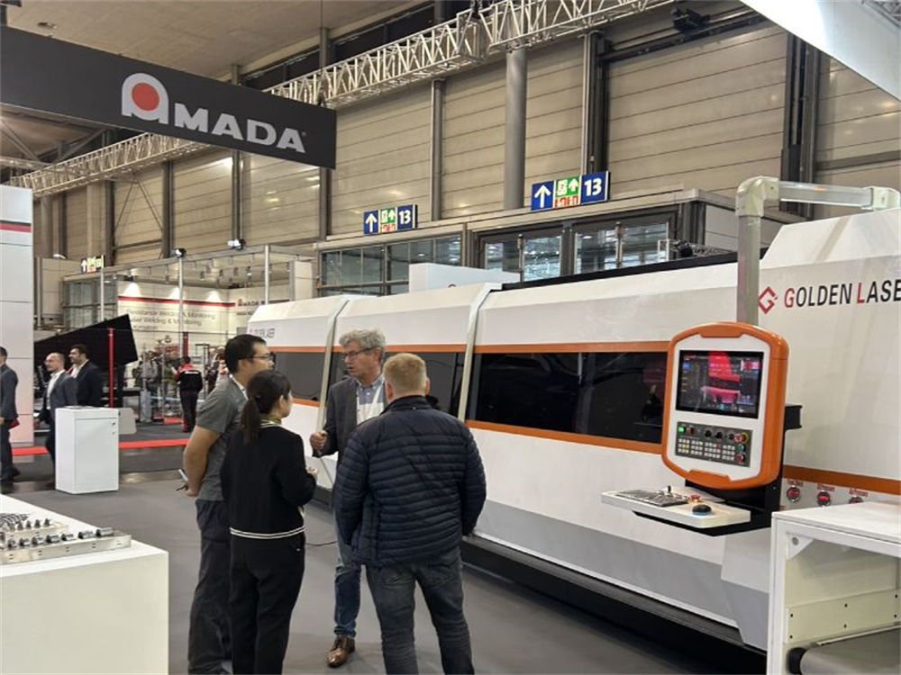 Attendees discussing laser cutting technology at an exhibition booth featuring Amada and Golden Laser machinery