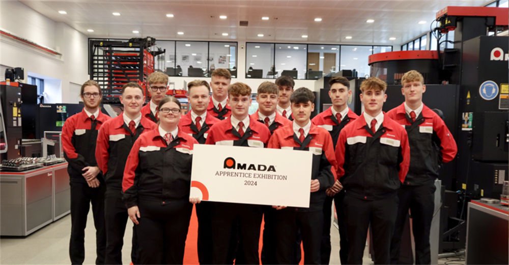 A group of apprentices in red and black uniforms holding a sign for the "Amada Apprentice Exhibition 2024.
