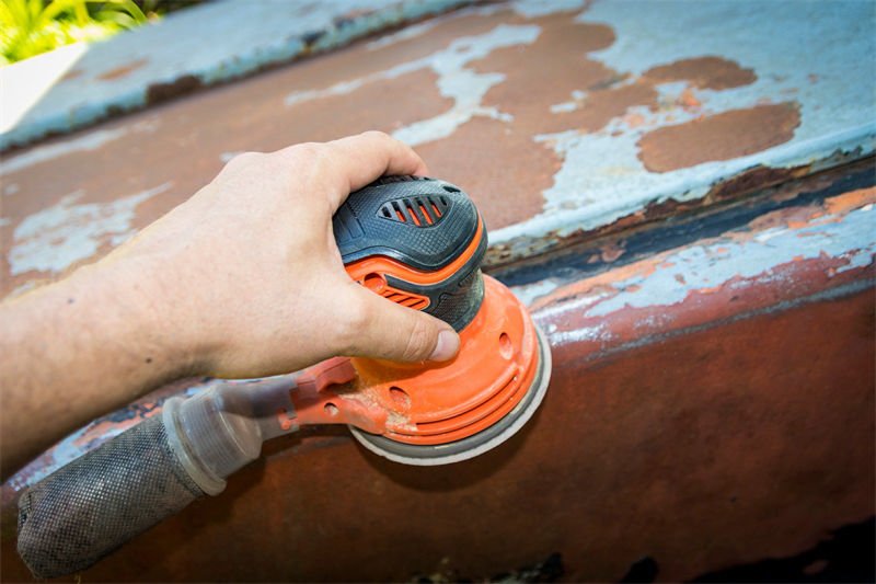 A person using an orbital sander to remove rust from a metal surface