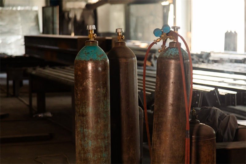 Several old oxygen cylinders lined up near laser cutting equipment in an industrial setting