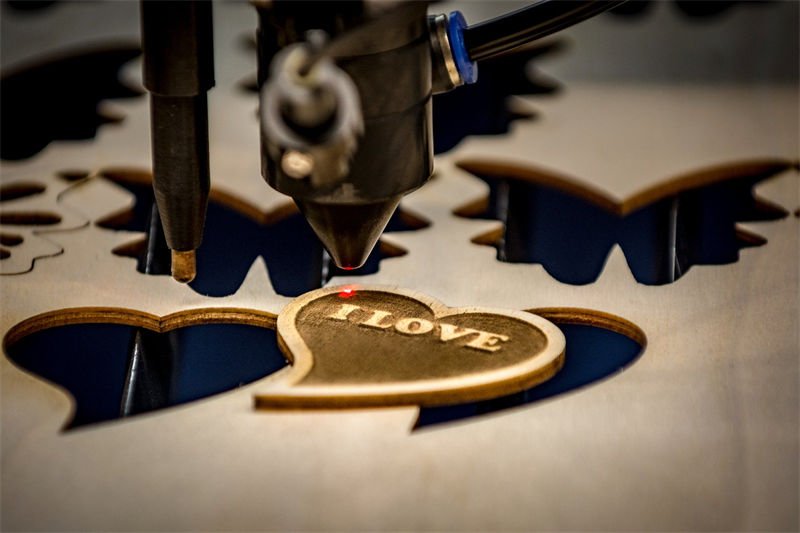 A CO2 laser engraver precisely engraving "I LOVE" on a wooden heart