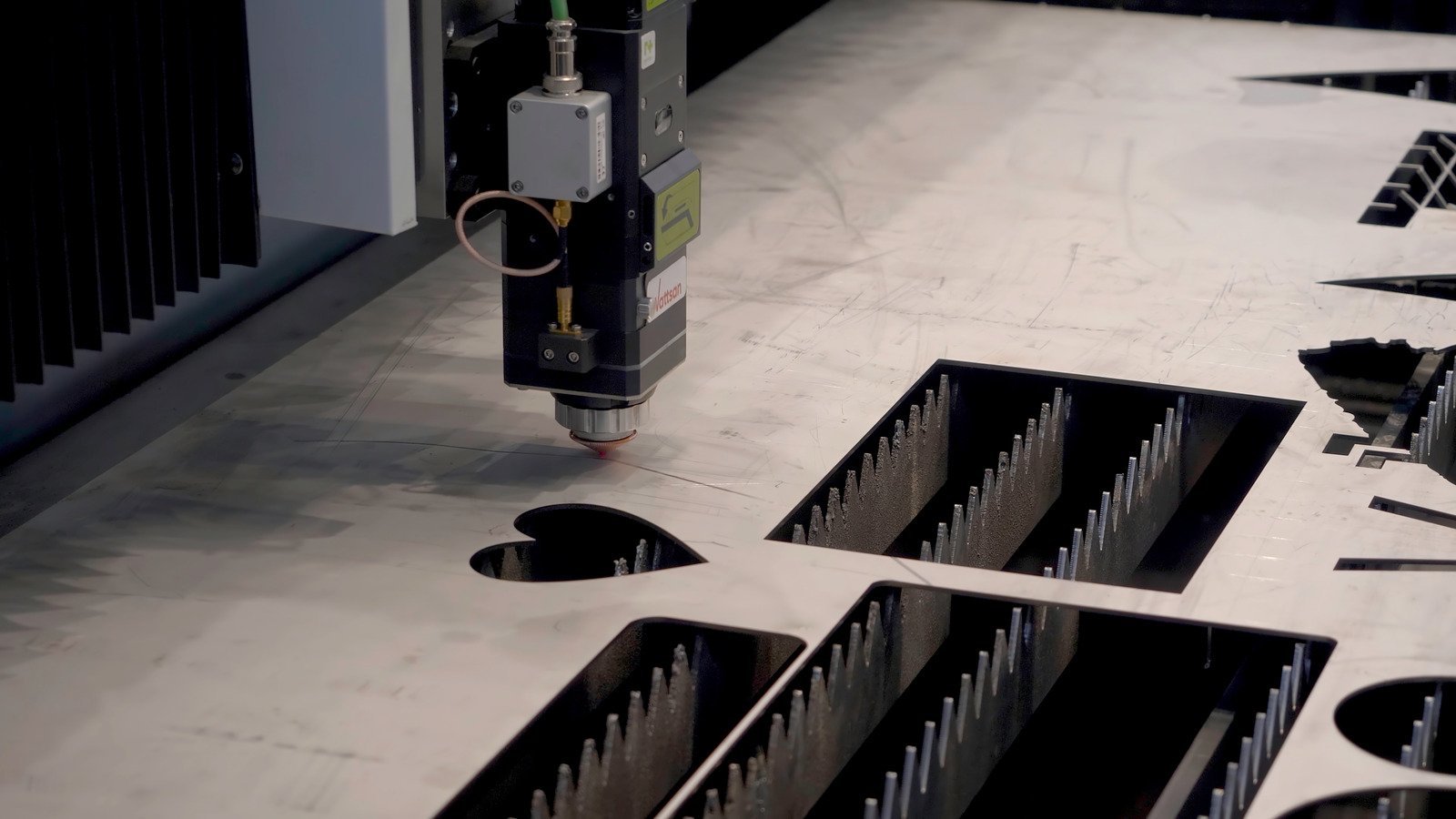 A laser cutting machine works on a metal sheet with intricate cut-outs, with a focus on the machine's precision head