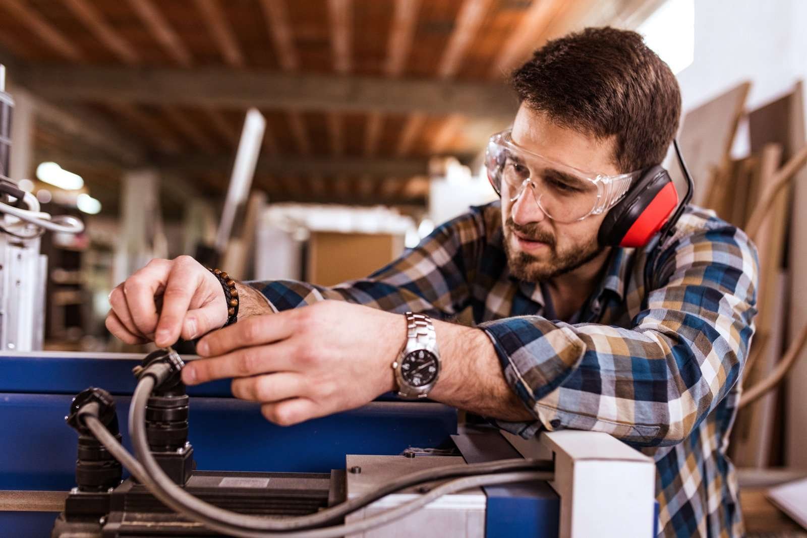 A laser engraver operator wearing safety goggles and earmuffs while adjusting equipment