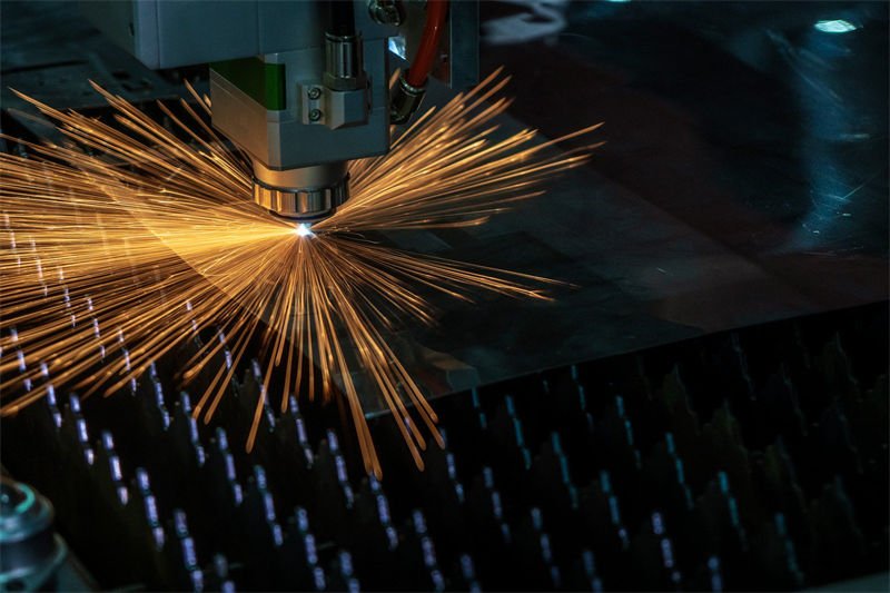 Close-up of a laser cutting machine emitting a radial spray of sparks while cutting a metal sheet