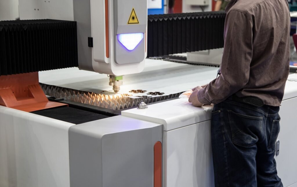 A technician observes a modern laser cutting machine as it operates on a metal sheet, in a clean and advanced manufacturing setting.
