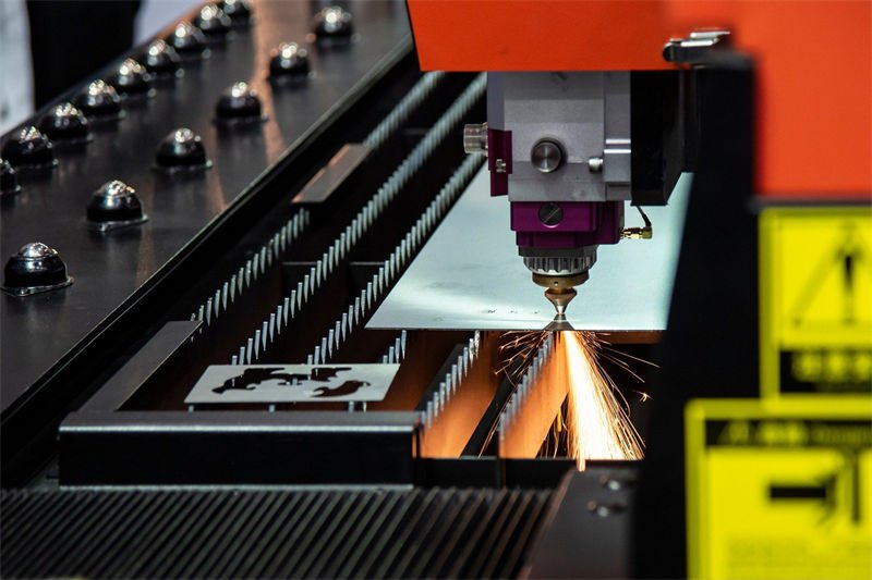 A laser cutter precisely slicing through an aluminum sheet, emitting bright sparks