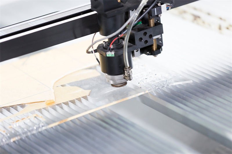 A laser cutter precision-cutting intricate shapes into an acrylic sheet on an industrial bed.
