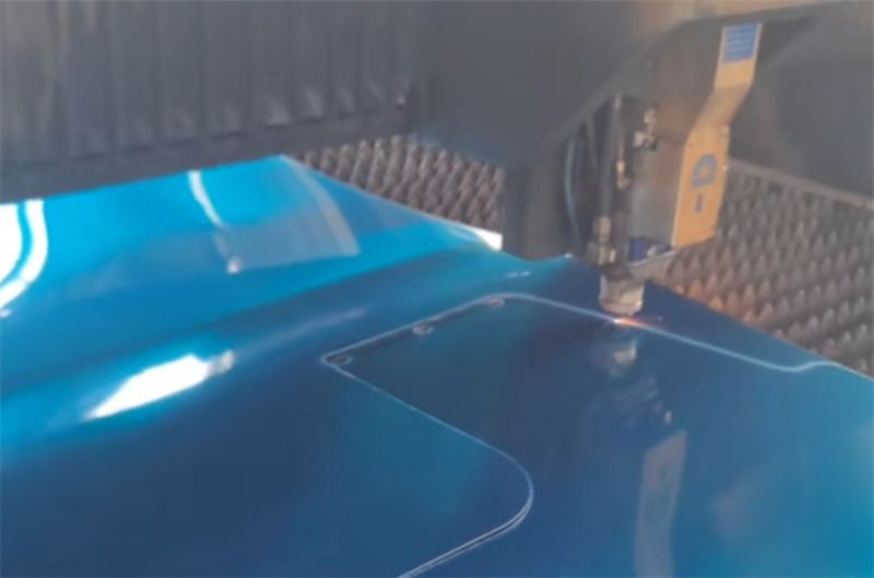 A laser cutting machine working on a blue coated metal sheet.