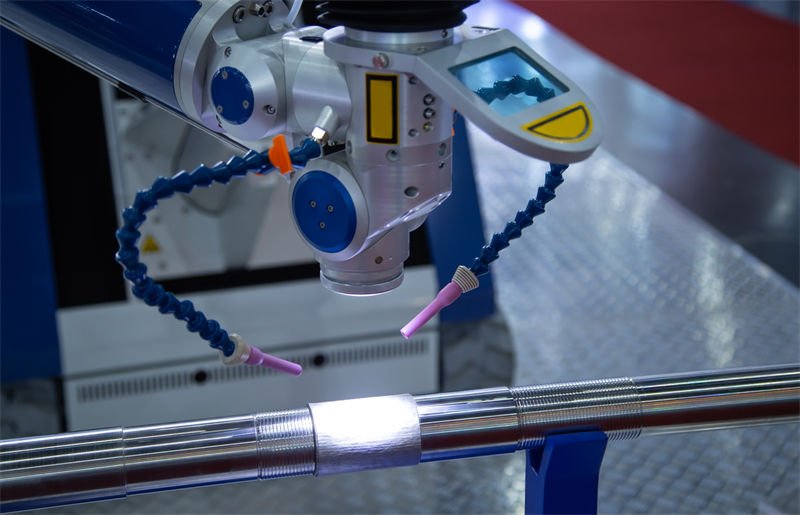 Precision laser welding equipment in action on a cylindrical metal component.
