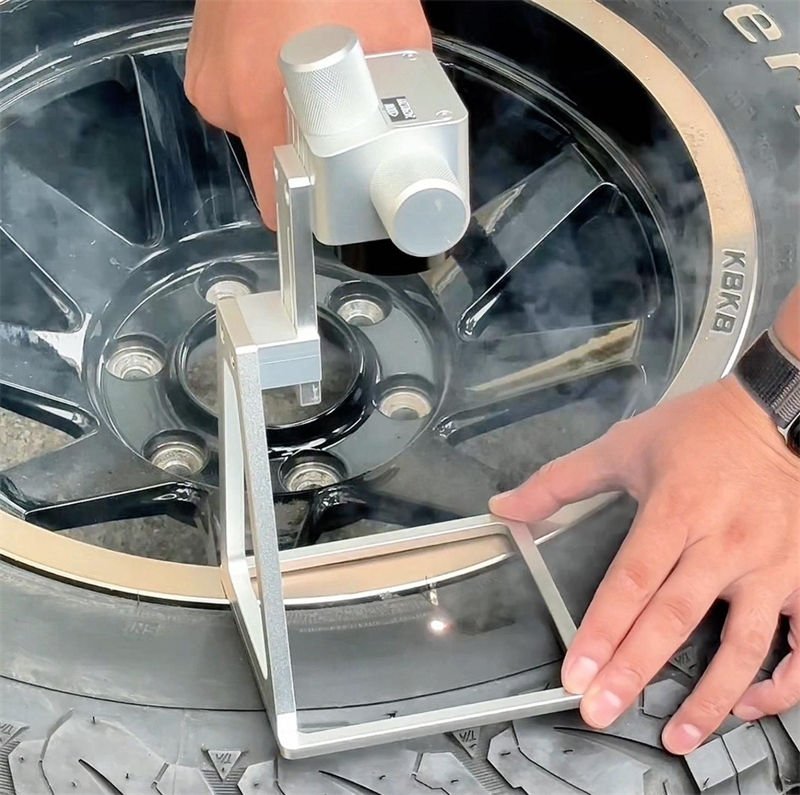 A handheld laser marking machine engraving a custom design on a tire and wheel rim