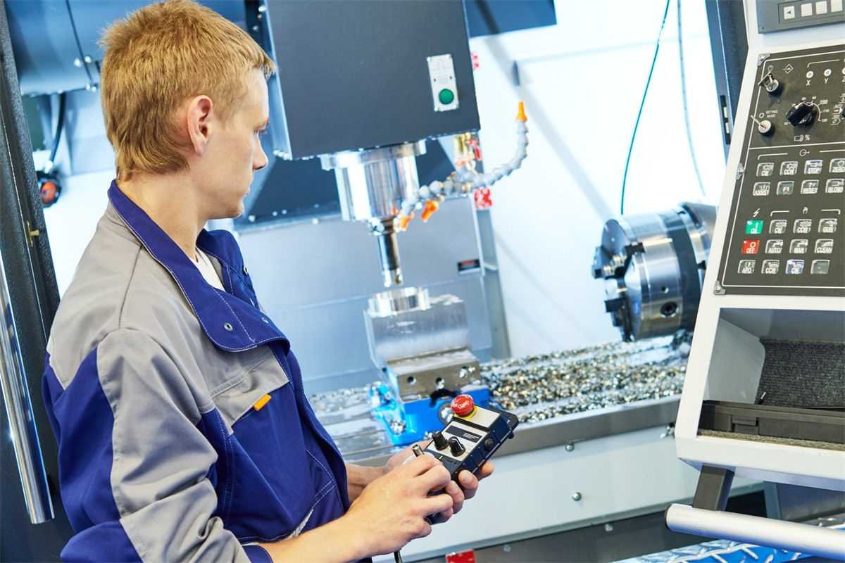 A technician using a handheld control pendant to manually operate a CNC milling machine in a clean industrial workshop