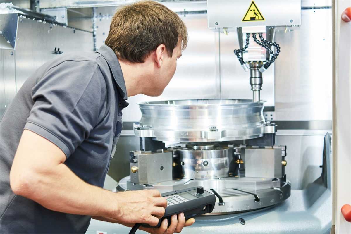 A technician using a handheld controller to inspect and adjust a CNC machine working on a large circular metal workpiece