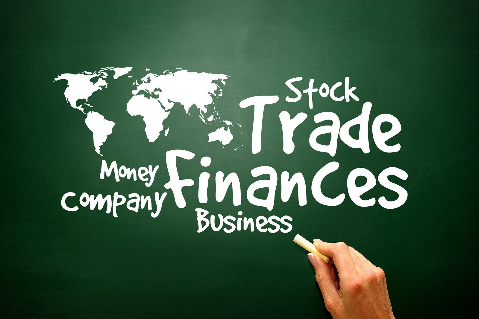 Global Finance and Trade Concepts on a Chalkboard A hand holding a piece of chalk writes financial terms such as