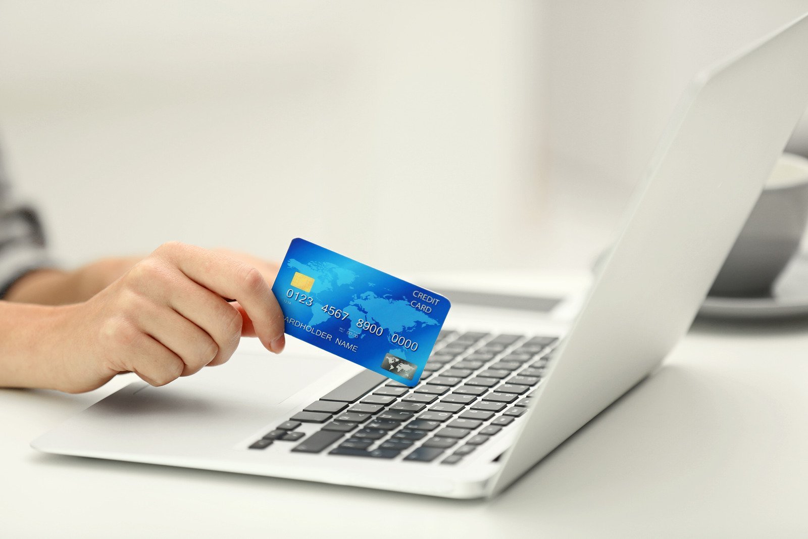 A person holding a blue credit card near a laptop keyboard, representing online financial transactions or bulk payment processing