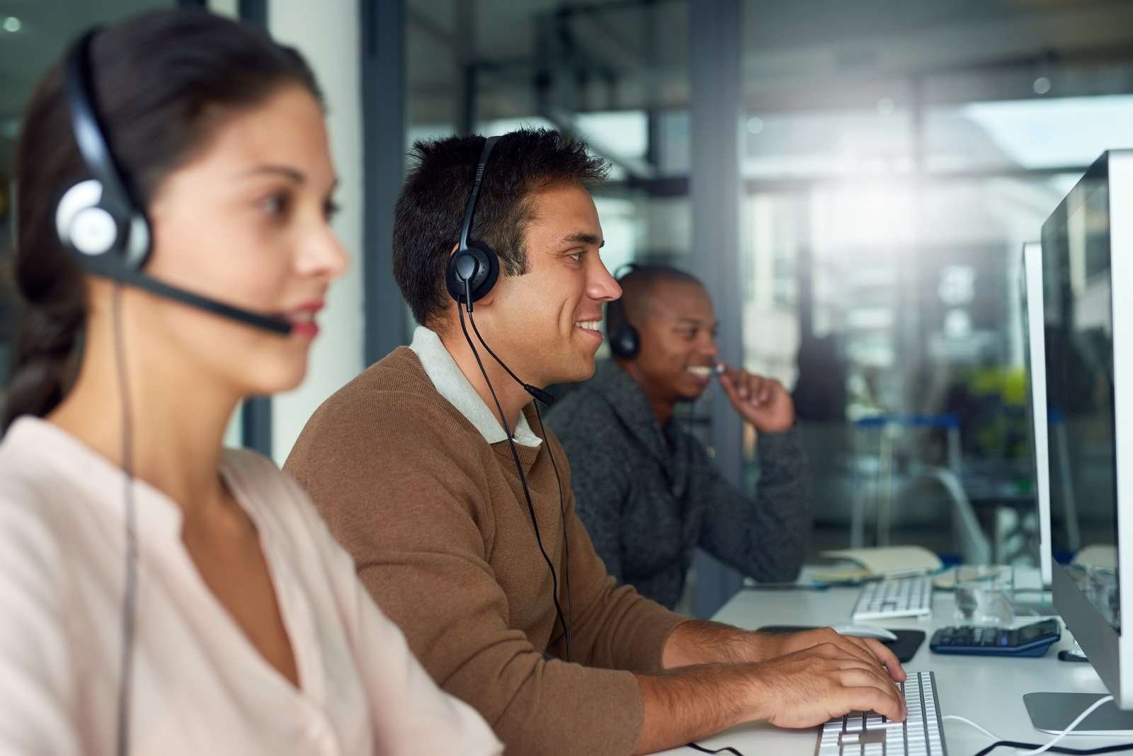 Customer service representatives wearing headsets, working at computers in a modern office environment