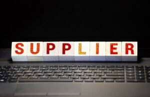 Wooden blocks spelling "SUPPLIER" placed on a laptop keyboard, symbolizing the selection of suppliers