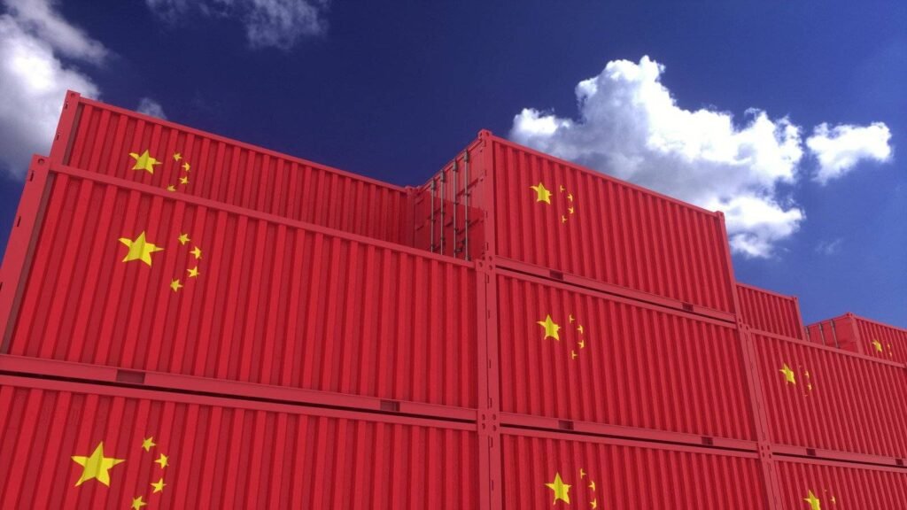 Stacked red shipping containers with the Chinese national flag against a clear blue sky